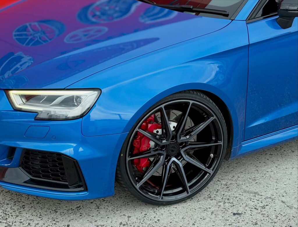 Close-up of a dark multi-spoke alloy wheel and red brake caliper on a blue Audi at Tyreforce.