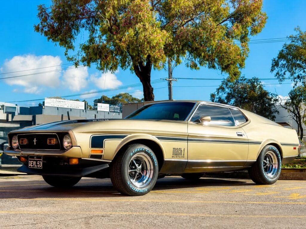 Gold classic Ford Mustang Mach 1 with polished-lip wheels and white-letter tyres.